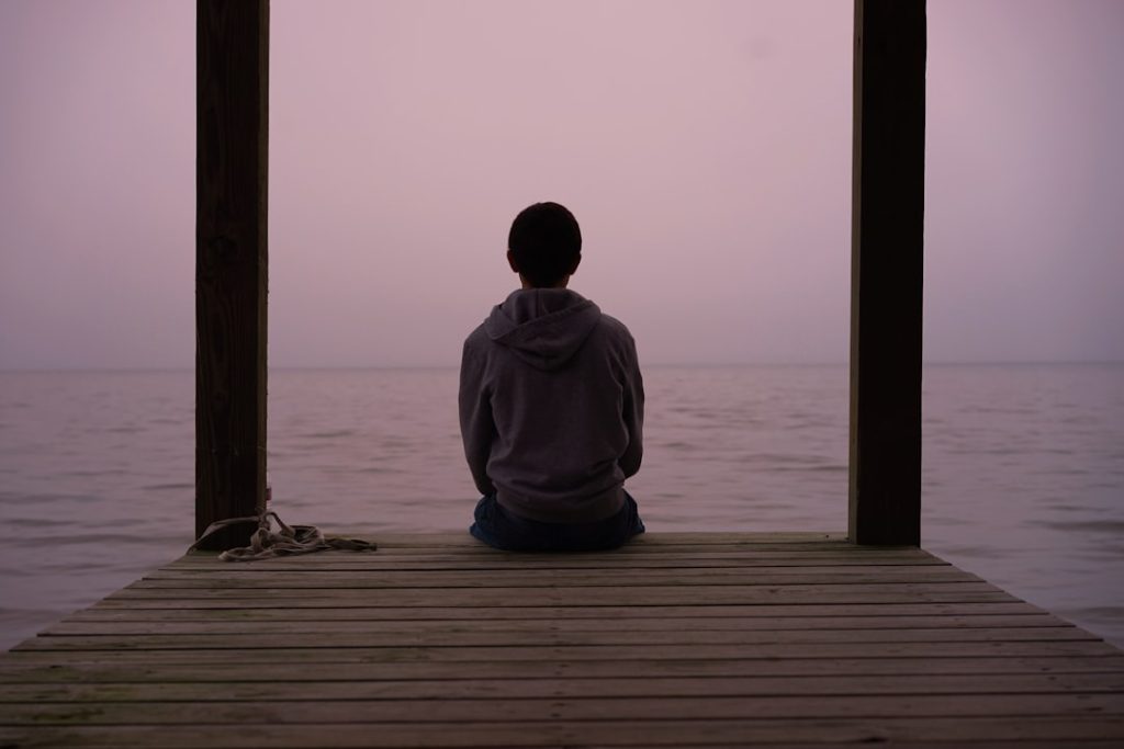 Person sitting alone on a dock above the water